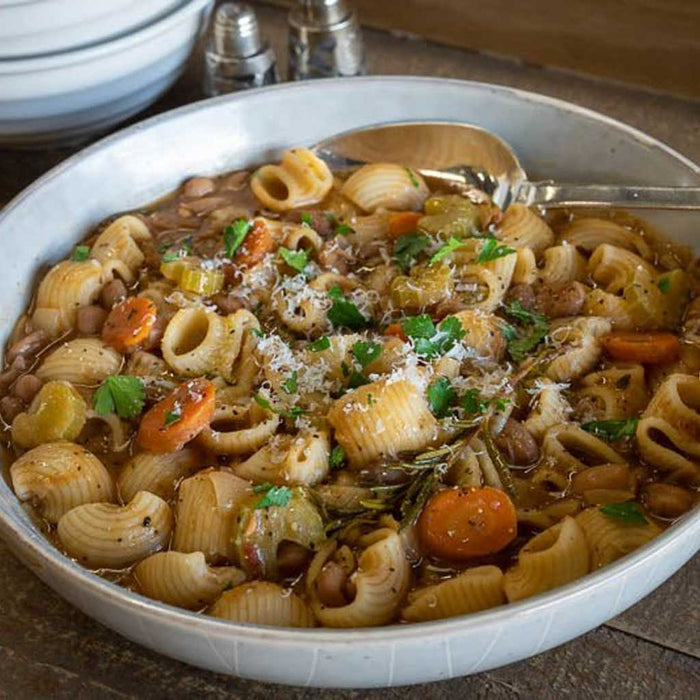 Pasta dish with beans in a white bowl on a wooden surface