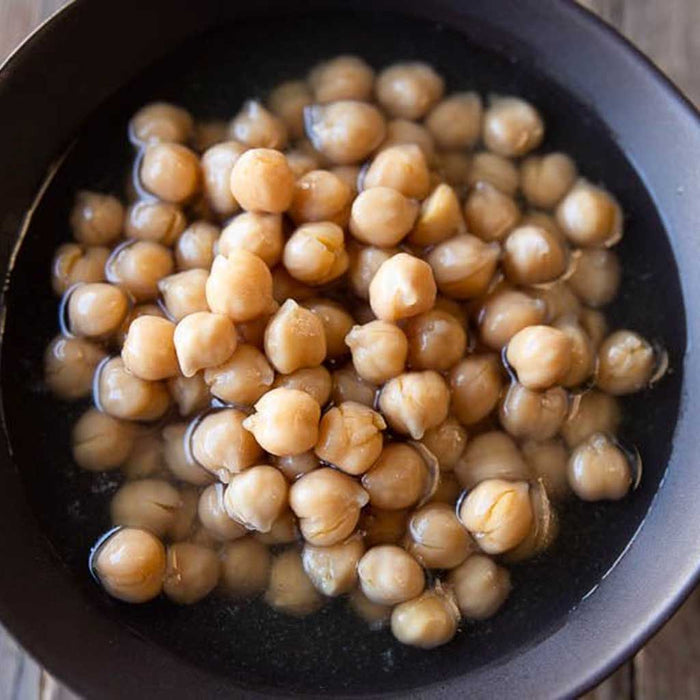 Chickpeas soaking in a dark bowl on a wooden surface