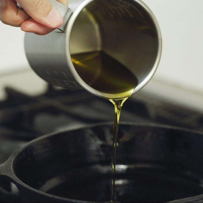 Olive oil being poured from a measuring cup into a pan.