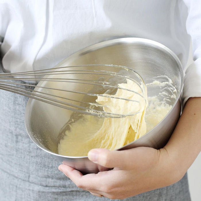 Person whisking batter in a metal bowl with a white background