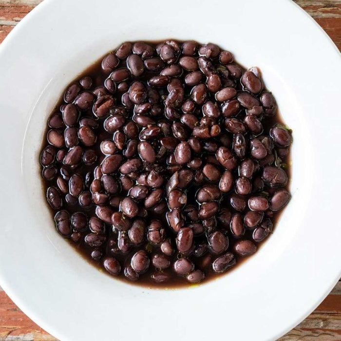 White bowl filled with black beans on a wooden surface