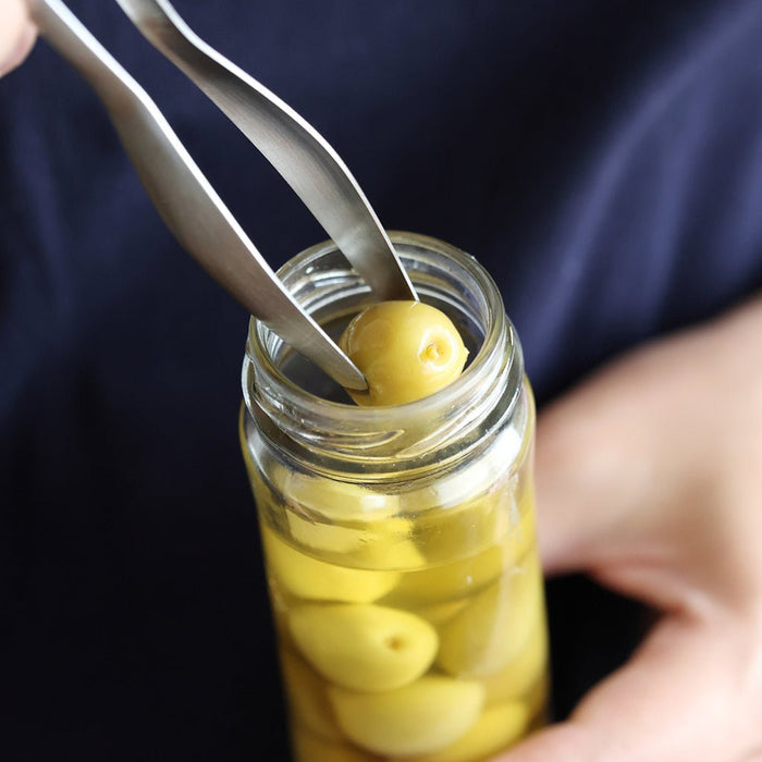 Person using tongs to pick up an olive from a jar.