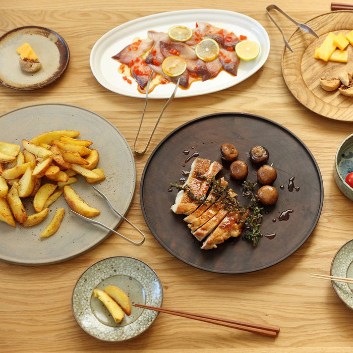 Diverse food dishes on a wooden table including meat, fries, and vegetables with chopsticks and tongs