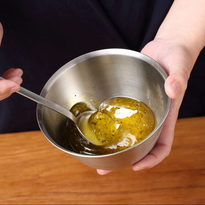 Metal bowl with olive oil and herbs, held by a person on a wooden surface.
